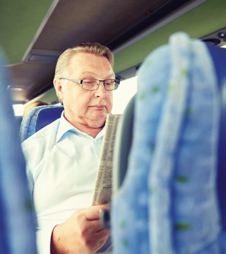 happy senior man reading newspaper in travel bus